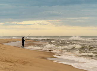 A man fishing from the beach at sunset
