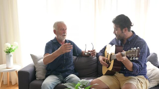 adult son playing guitar to sing a song with senior father, having fun and happy at home, family concept with music art together