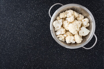 Bowl of chopped up cauliflower on a black cutting board
