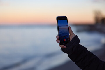 Hand holding phone and recording sunset over lake Erie. 