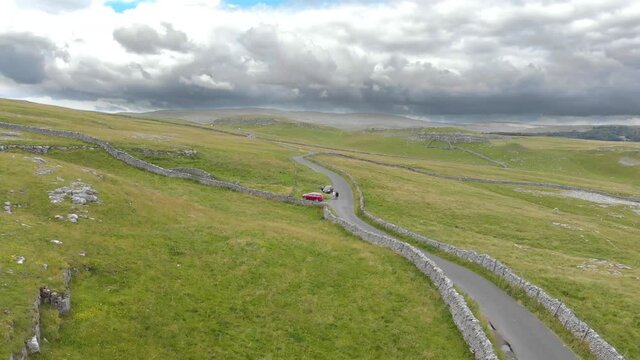 long paved road alongside bumpy green hills atop Malham Cove, North Yorkshire, England on cloudy day. drone pedestal shot