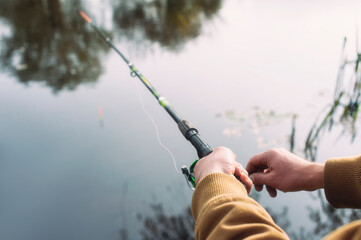 Man fisherman catches a fish on a fishing rod with a reel on the lake against the background of the forest and sky with clouds.