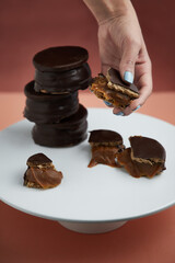 Torre de alfajores rellenos de dulce de leche bañados en chocolate mano sosteniendo un trocito de alfajor