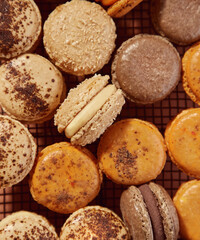 vista cenital de macarons franceses beige, naranja y marron sobre rejilla negra de alambre en fondo de terracota
