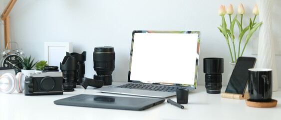 Graphic design and photographer workspace concept with blank screen laptop mock up, medium format camera, digital tablet and photographer equipment.