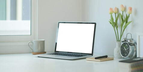 Simple workspace with white screen laptop, coffee cup and notebook on white table.