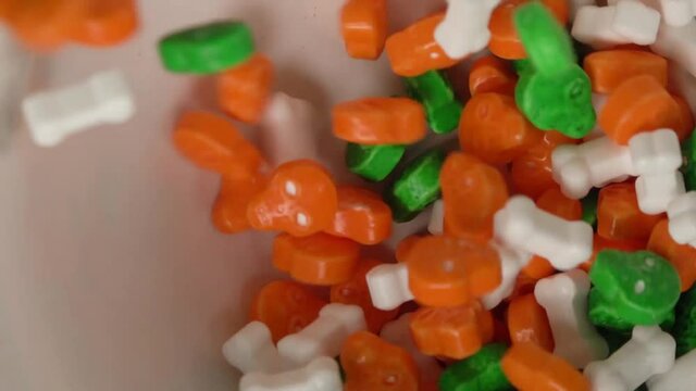Orange and green skulls and bones shaped candy falling on a plate.