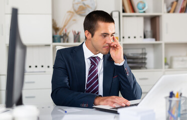 Naklejka premium Portrait of troubled businessman looking worriedly at laptop screen in office..