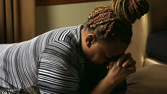 Black woman on knees in living room praying to God without ceasing Prayer for our nation and world