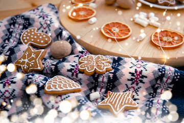 Knitting sweater, Christmas cookies, garland, marshmallows and dried oranges on a wooden circle. Cozy Christmas composition