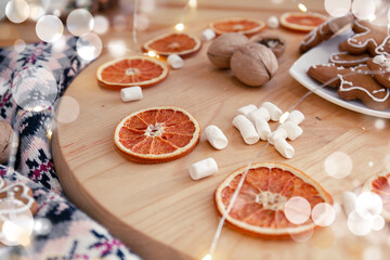 Knitting sweater, garland, marshmallows and dried oranges on a wooden circle. Cozy Christmas composition