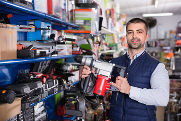 Adult friendly smiling positive male is standing with puncher in tools store.