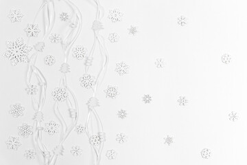 Christmas white background made of white wooden snowflakes and small Christmas trees and round beads on narrow ribbons.