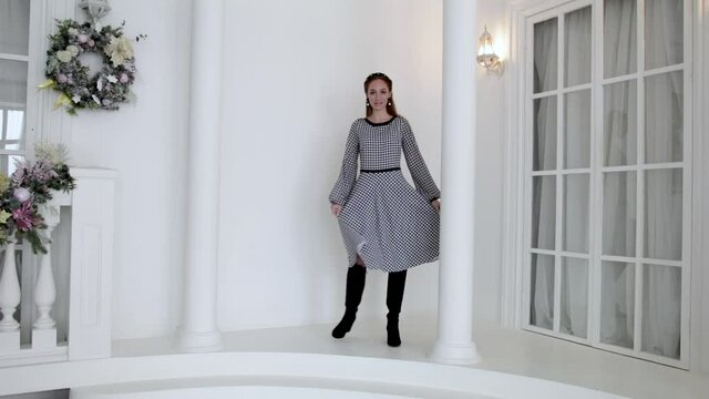 elegant young girl in a dress posing next to a column and a large window of the house, slow motion