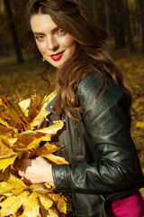 Young brunette woman portrait in autumn color. Yellow leaves in her hand.