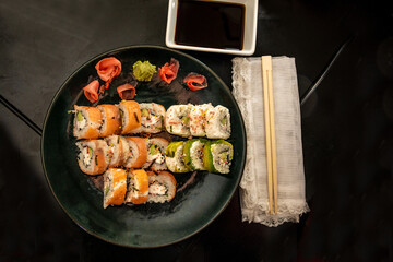 Sushi of different variants served with soy sauce and chopsticks, on a green plate