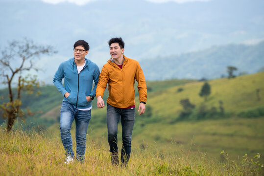 Portrait Of Two Asian Man Friends With Hiking Together On Grass Hill In Autumn. Happy Male Gay Couple Relax And Enjoy Walking On Mountain Trail. Healthy Outdoor Lifestyle Holiday Vacation Concept.