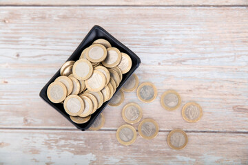 Small plate full of euro coins and scattered coins on the table