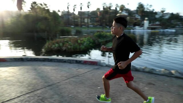 14 year old boy jogs around a small lake in Los Angeles. Los Angeles skyline can be seen in the distance.
