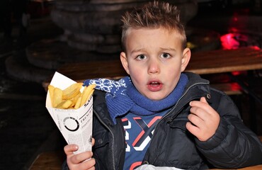 Retrato de chico rubio comiendo un cucurucho de patas fritas - obrazy, fototapety, plakaty