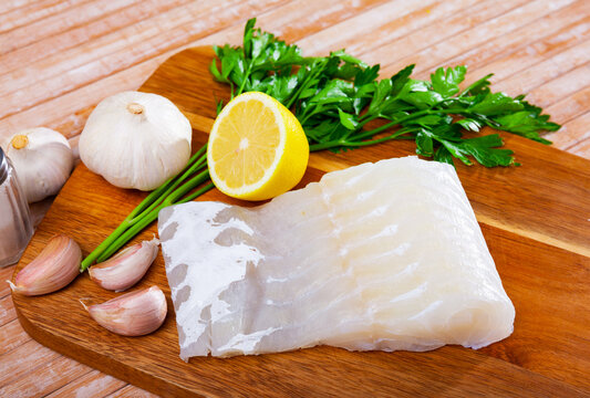 Piece of fresh rockling fillet on wooden surface with seasonings prepared for cooking