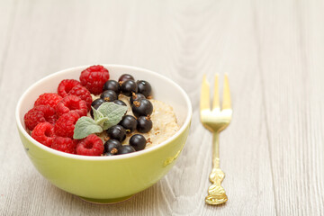 Oatmeal porridge in porcelain bowl with currant berries and raspberries