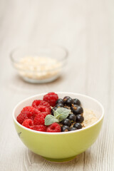 Oatmeal porridge in porcelain bowl with currant berries and raspberries
