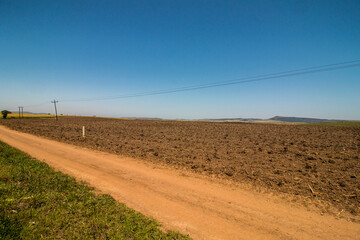 Fototapeta na wymiar Newly Ploughed Field Against Blue Sky Bordered by Dirt Road