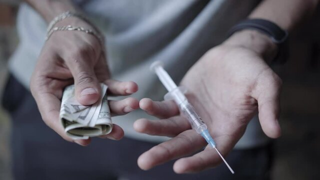 Top view of male teenage hands holding syringe and pack of dollars. Unrecognizable mixed-race addicted boy with narcotics and money. Narcomania and drug trafficking.