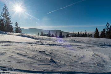 Winter mountain scenery with snow, trees, hills on the background and clear sky wih sun on Cienkow mountain ridge in Beskid Slaski mountains in Poland