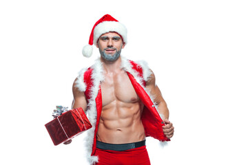 Sexy Santa Claus. Bodybuilder young handsome santa clause smile holds a gift in a red box and shows off abs cubes at New Years eve and Christmas winter holiday white background.