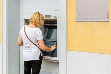 Fototapeta na wymiar Blond white woman withdraws cash from an ATM