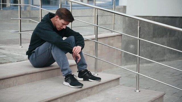 Tired man in sportive clothes sitting on the stairs and then runs away.