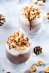 Cold winter chocolate dessert with whipped cream, popcorn and caramel topping in glasses on beige background, place for text