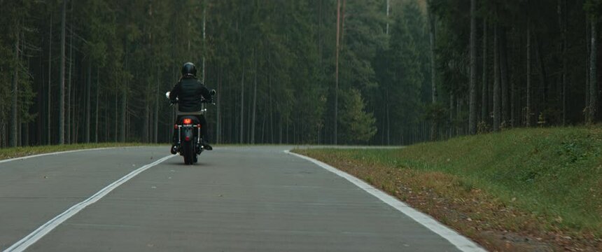 WIDE BACK VIEW TRACKING Biker riding his custom built vintage retro motorcycle on a scenic forest road. Shot on RED cinema camera with 2x Anamorphic lens