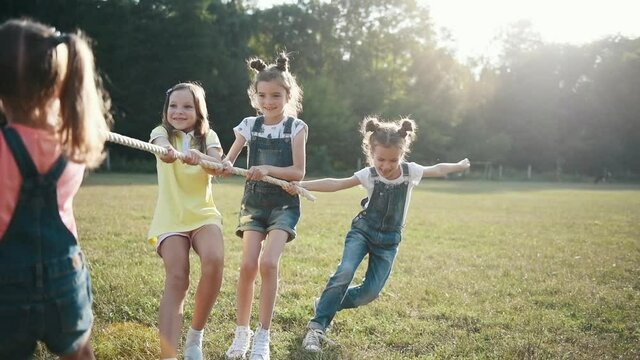 Kids having fun by playing tug of war game on the field at sunny daytime.