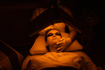 Young woman having yellow LED light facial therapy treatment in beauty salon. Beauty and wellness