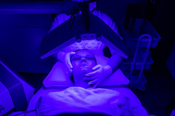 Young woman having blue LED light facial therapy treatment in beauty salon. Beauty and wellness