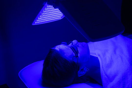 Young woman having blue LED light facial therapy treatment in beauty salon. Beauty and wellness