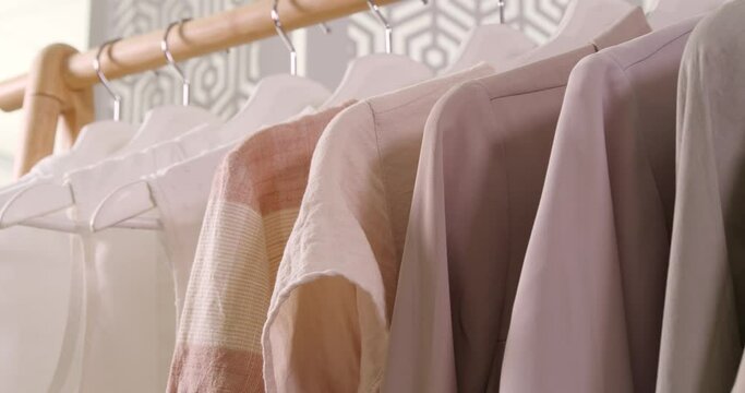 Viewing stylish garments on hangers, closeup. Camera moving backward along wooden clothes rack