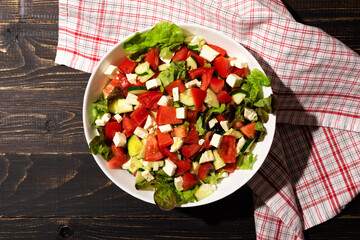 Organic vegetable salad of fresh lettuce, tomato, cucumber and cheese. Bowl of healthy diet meal on wooden table. Top view, copy space