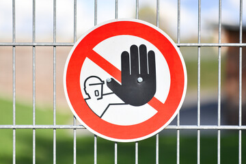 Red round 'Keep out' warning sign with person holding up hand in red circle at fence protecting...