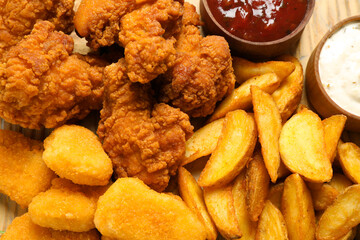 Tasty deep fried chicken pieces and nuggets with garnish as background, top view
