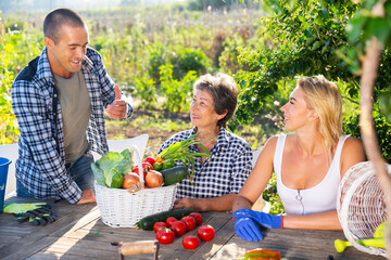 Portrait of positive family of adult gardeners talking in garden after harvesting vegetables