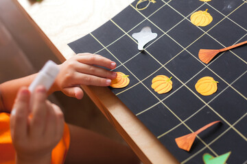 Preschooler boy making board game field for Halloween game, child sticks paper pumpkin