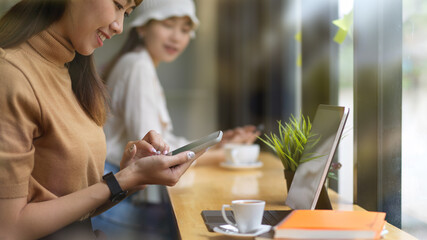 Fototapeta na wymiar Female teenager using smartphone and talking to her friend in cafe