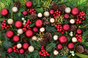 Christmas festive background scene with red & gold baubles & winter greenery of holly, ivy, mistletoe, cedar cypress leaves & pine cones. Xmas composition for the holiday season,. Flat lay, top view.