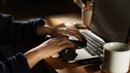 Female hand typing on laptop on wooden table with coffee cup