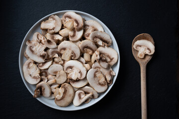 slices of champignon mushrooms on a plate. mushrooms over a dark background. plate of freshly cut sliced mushrooms.