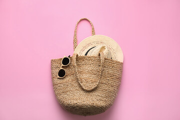 Elegant woman's straw bag with hat and sunglasses on pink background, top view